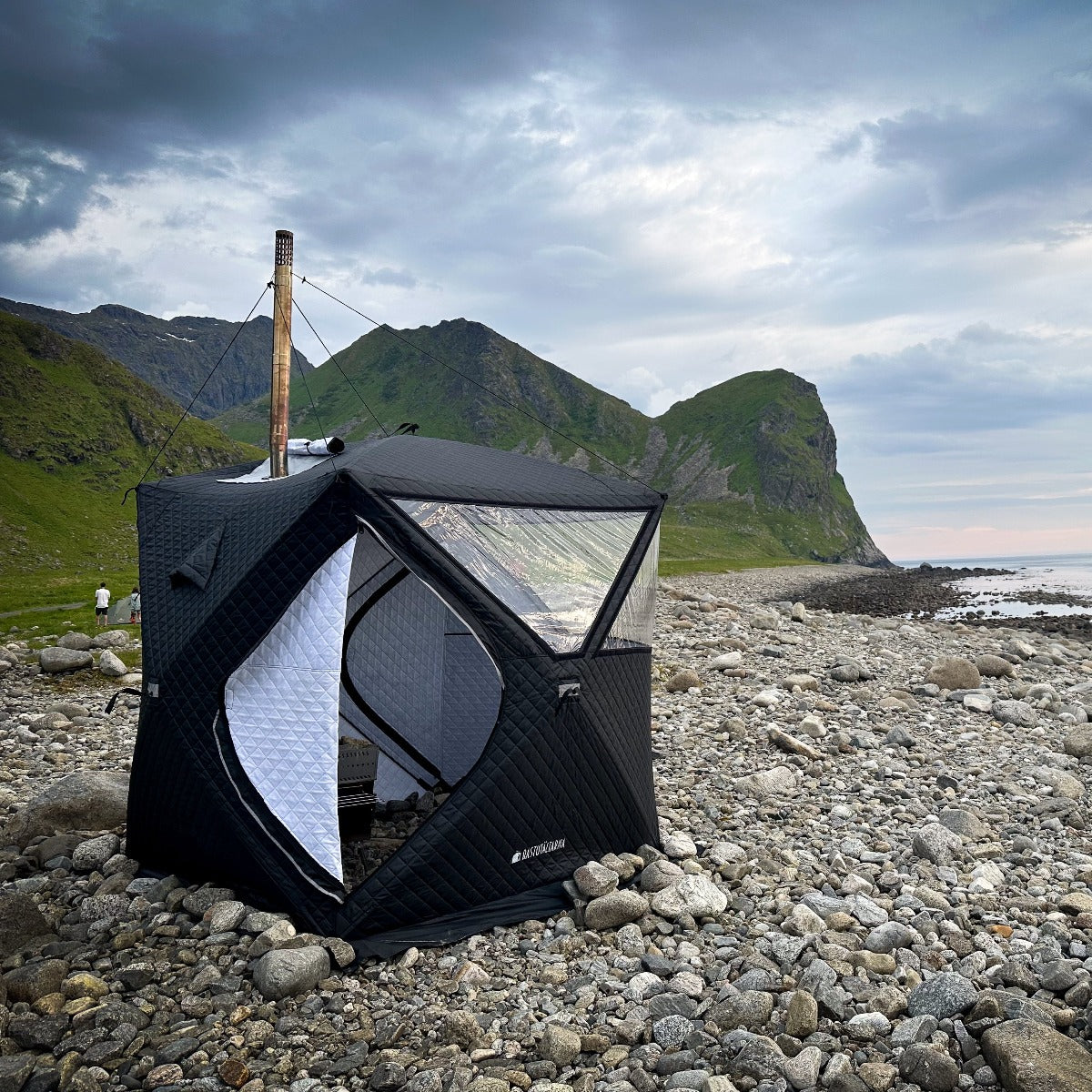 Batutält från Bastutältarna uppstält på en stenstrand på Lofoten medberg i bakgrunden