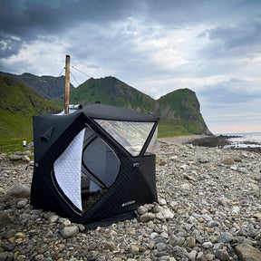 Batutält från Bastutältarna uppstält på en stenstrand på Lofoten medberg i bakgrunden