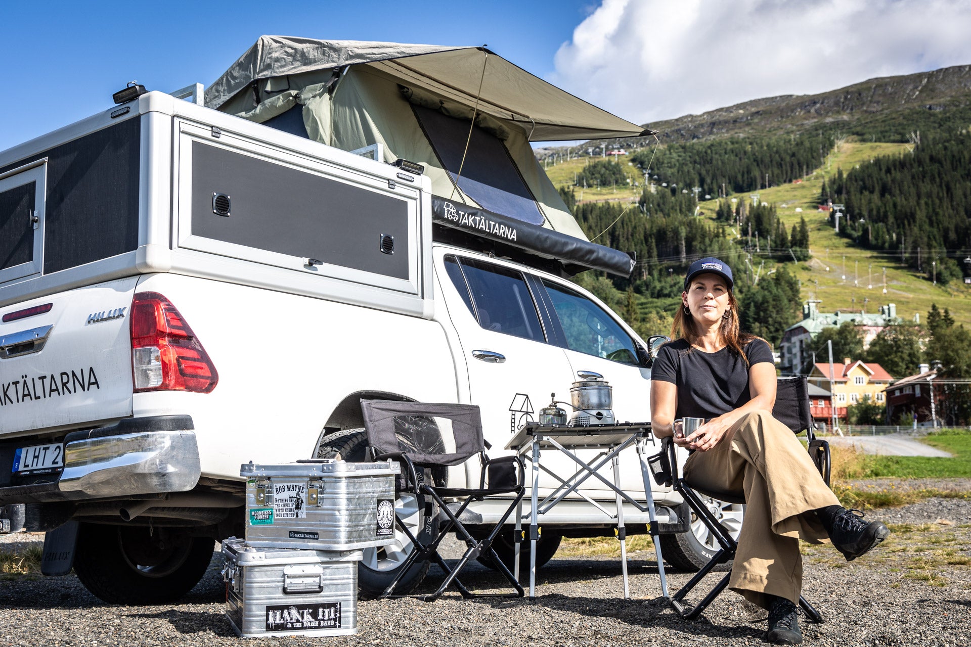 Elisabeth Standár, grundare av Taktältarna, sitter vid ett campingbord intill en bil med taktältet Åreskutan på och med berget Åreskutan i bakgrunden